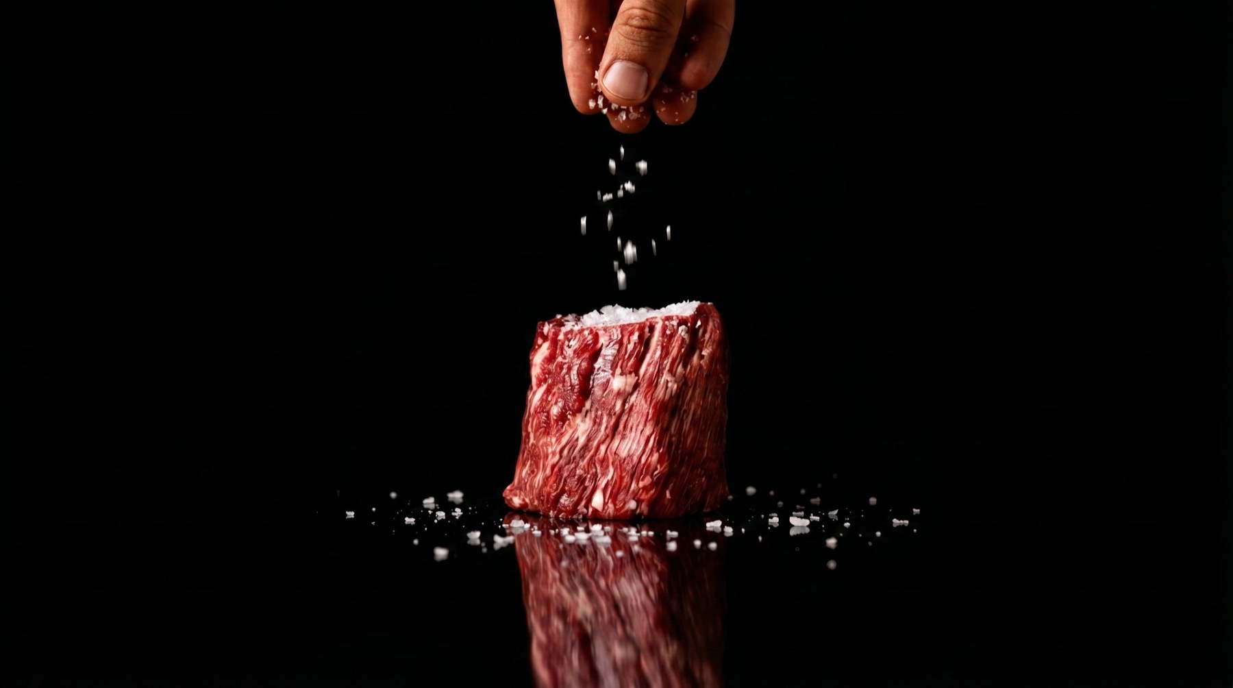 Una mano sala un cubo di carne, su fondo nero